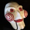 3D printed Jigsaw puppet mask with red spiral cheeks and red eyes inspired by the Saw horror movie.