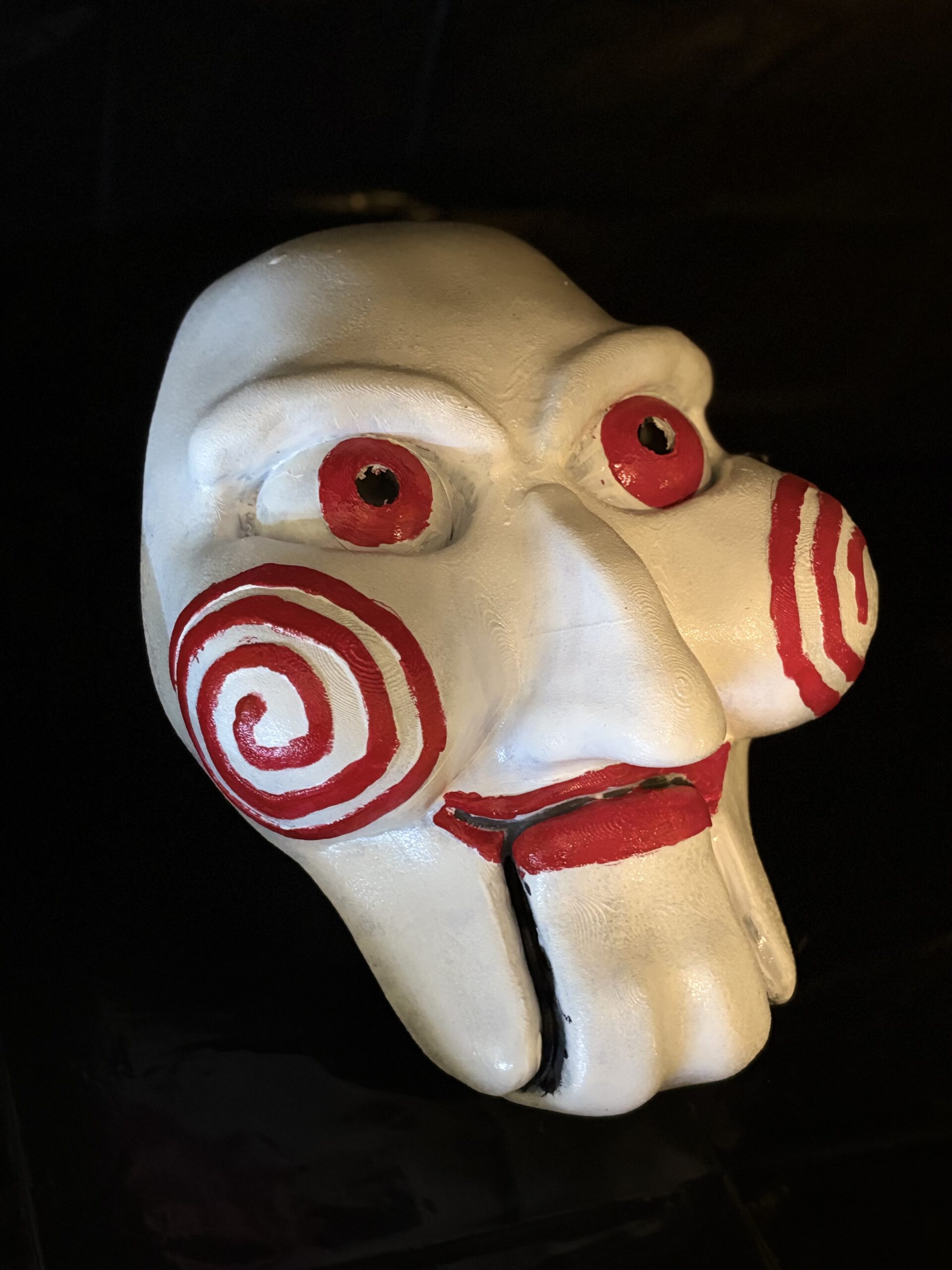 3D printed Jigsaw puppet mask with red spiral cheeks and red eyes inspired by the Saw horror movie.