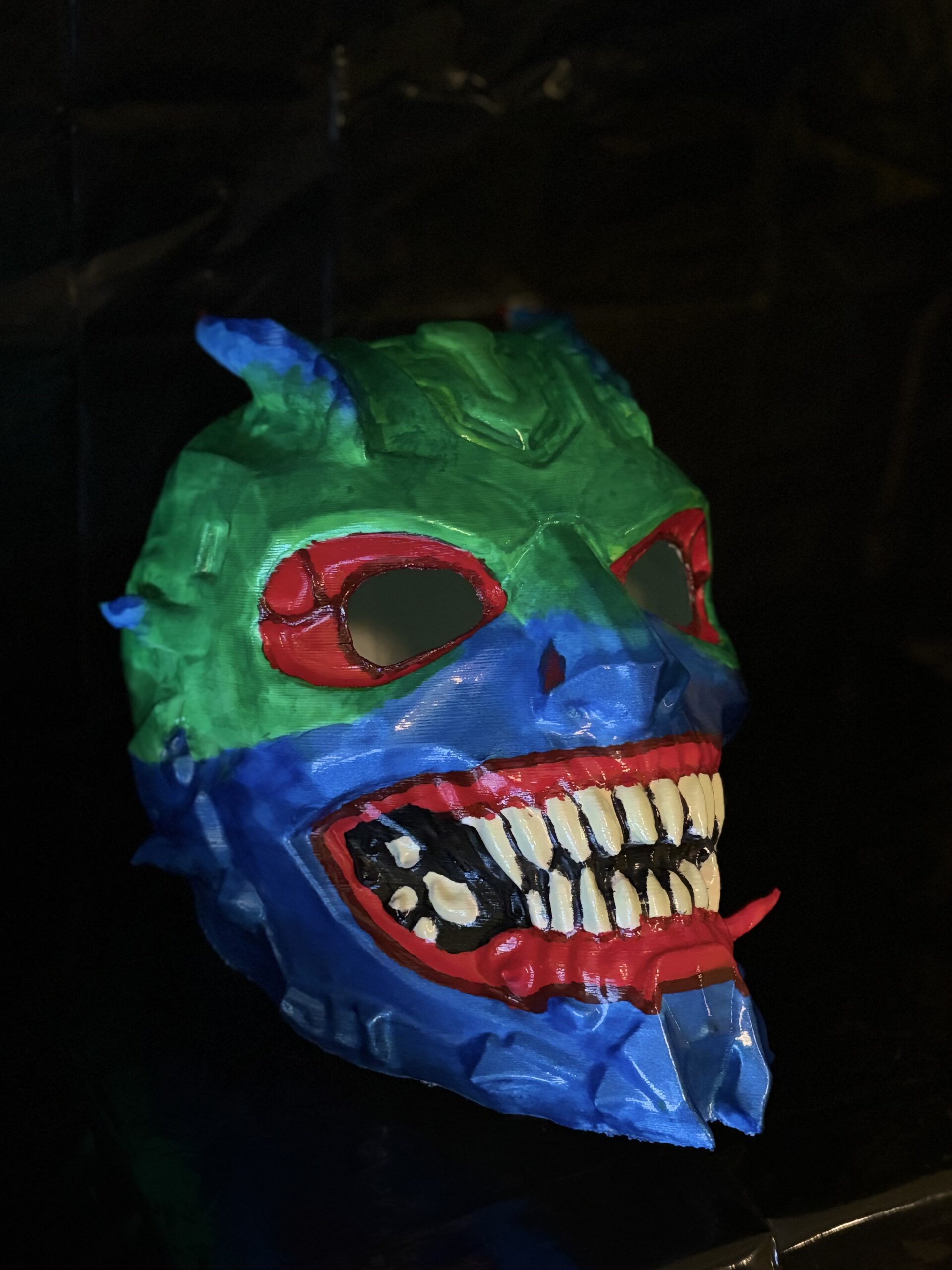 Hand-painted neon demon skull mask with sharp teeth and vibrant colors, 3D printed horror collectible.